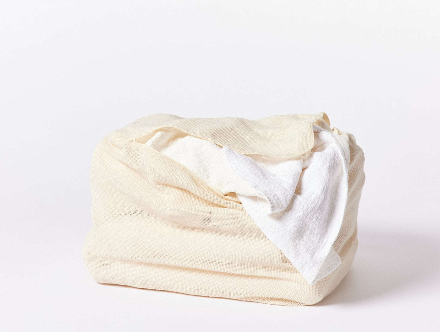 Coyuchi ivory cotton laundry bag folded with white fabric draped over top.