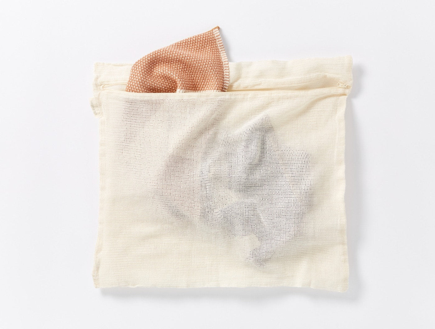 Coyuchi Conserve mesh laundry bag in natural, with a blush washcloth tucked inside.