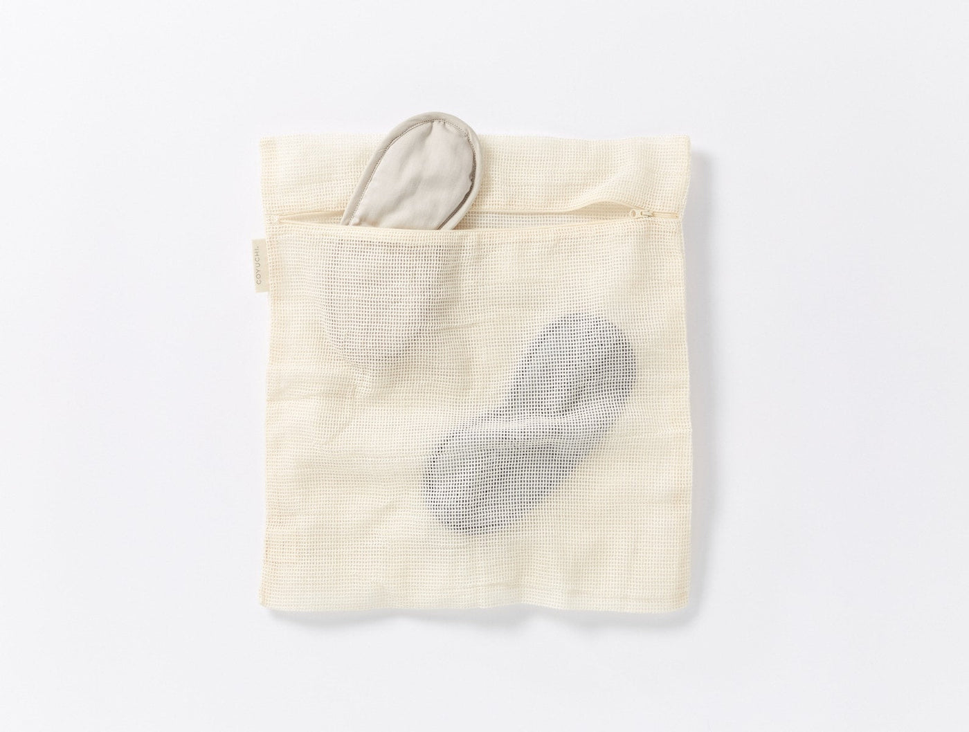 Coyuchi Conserve laundry bag in natural, with gray sleep mask tucked inside pocket.