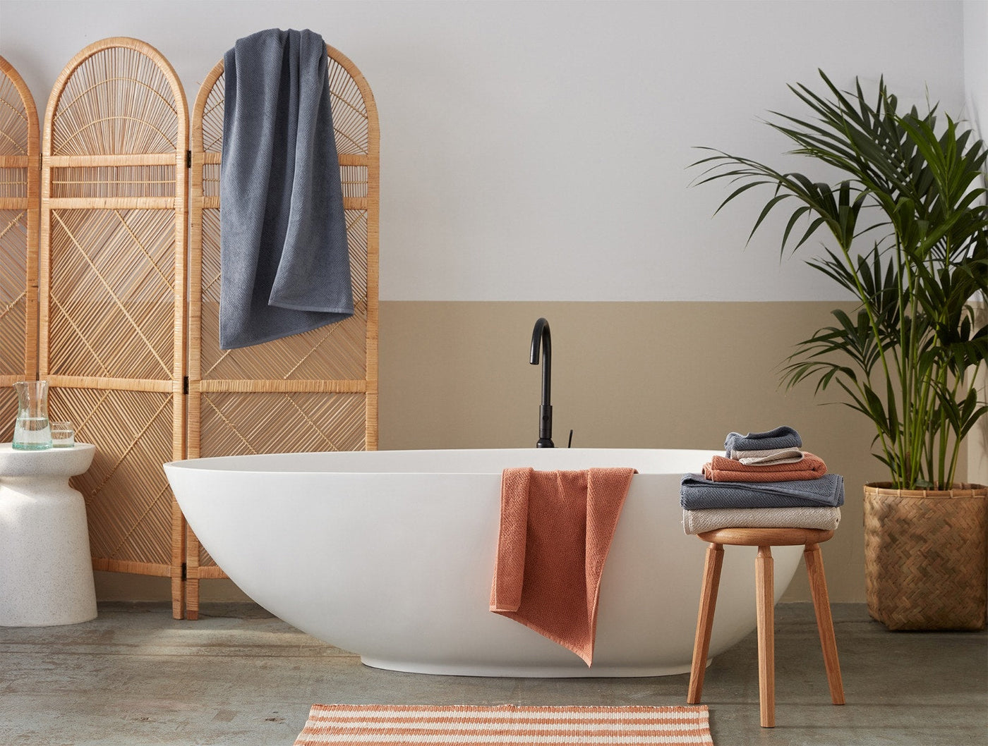 Coyuchi Air Weight towels in slate and terracotta draped over tub and stool in natural bathroom.