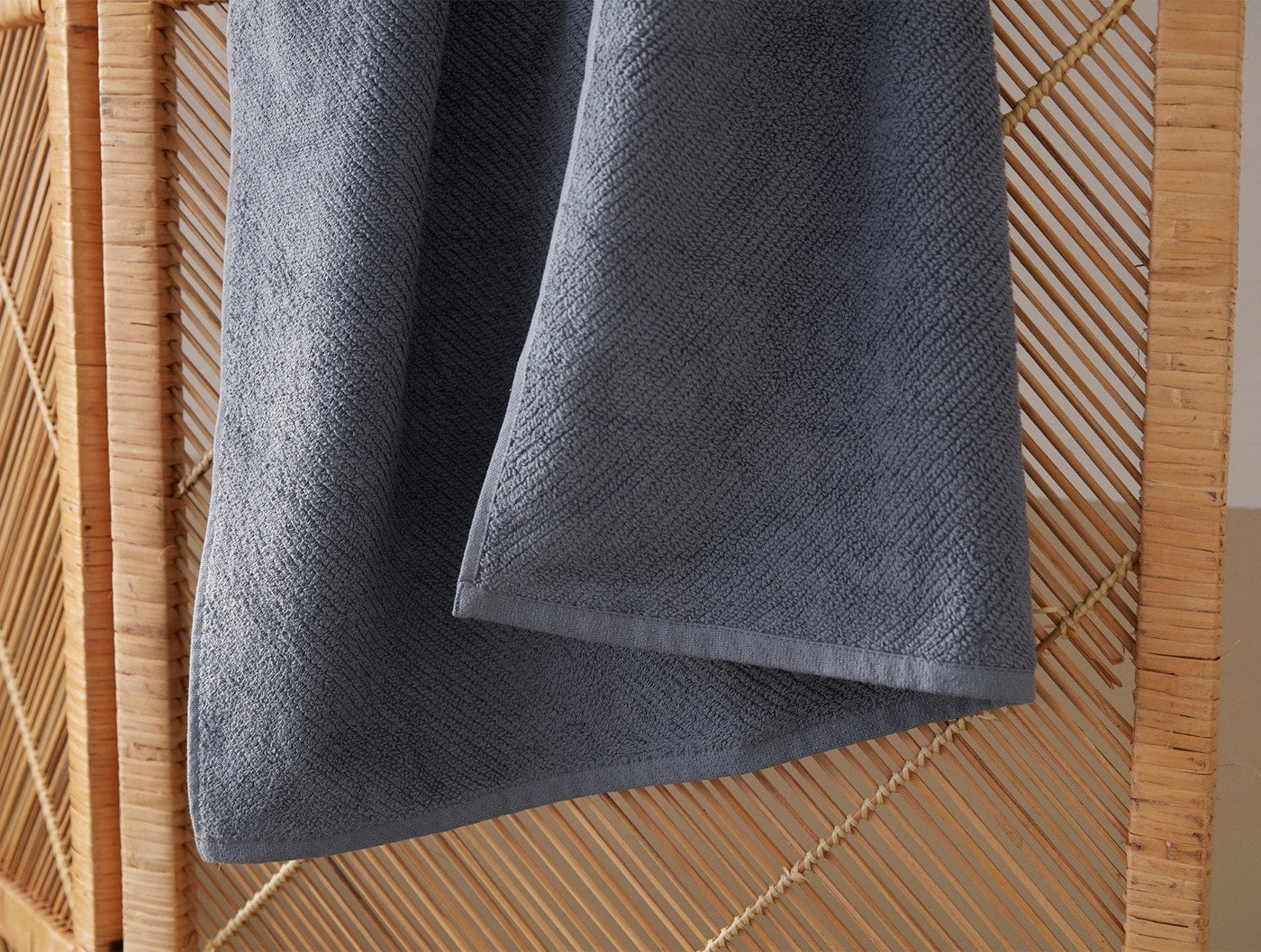 Slate grey wash cloth draped over a woven rattan surface, showing plush terry texture.