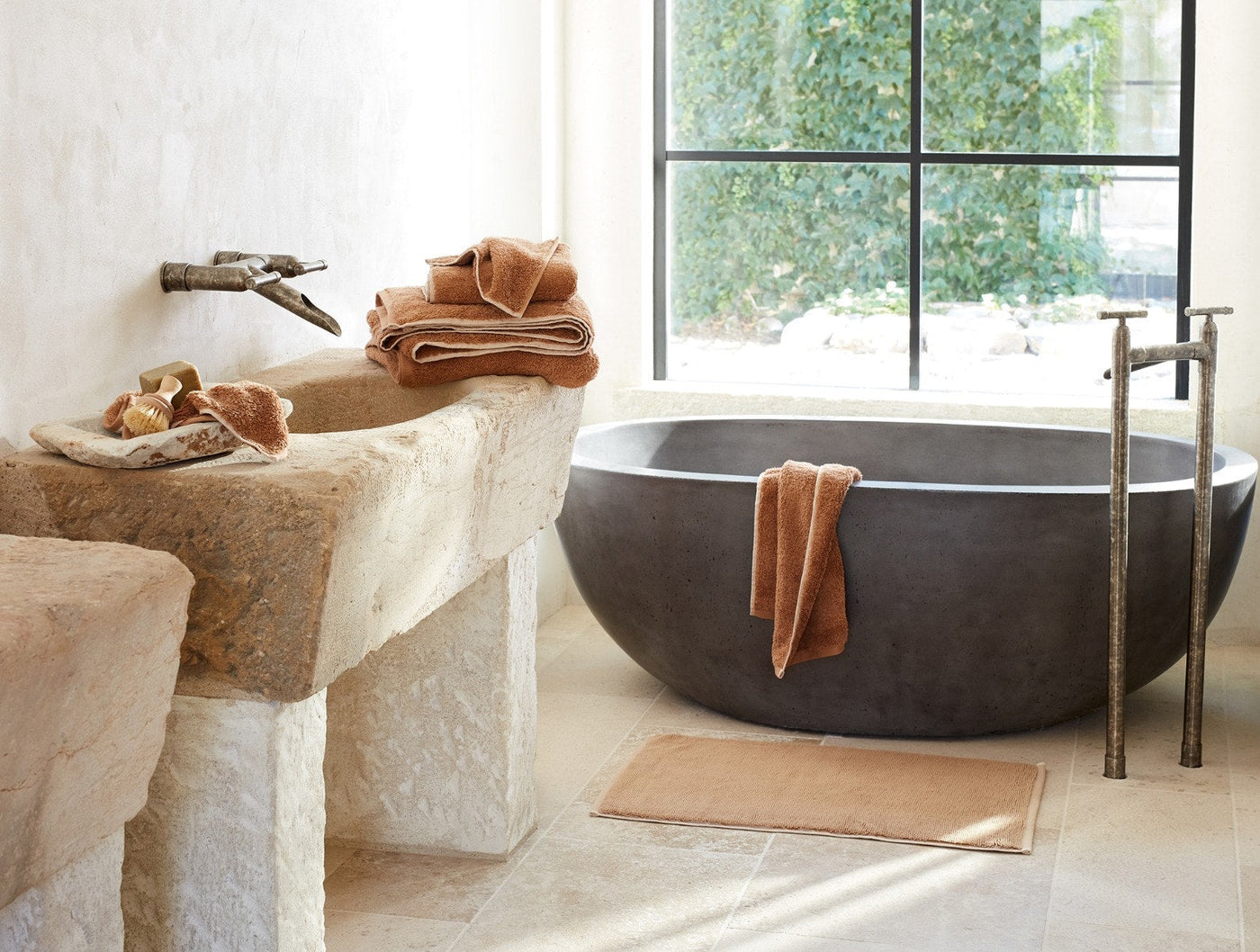 Coyuchi Cloud Loom towels in terracotta draped over stone tub and stacked on rustic sink.