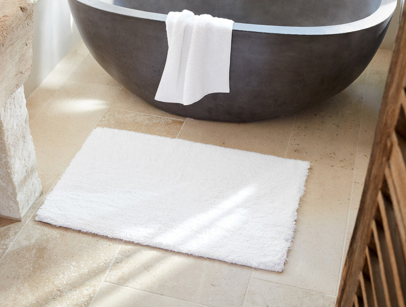 Coyuchi Shag bath rug in white, laid flat on stone tile floor beside a freestanding tub.