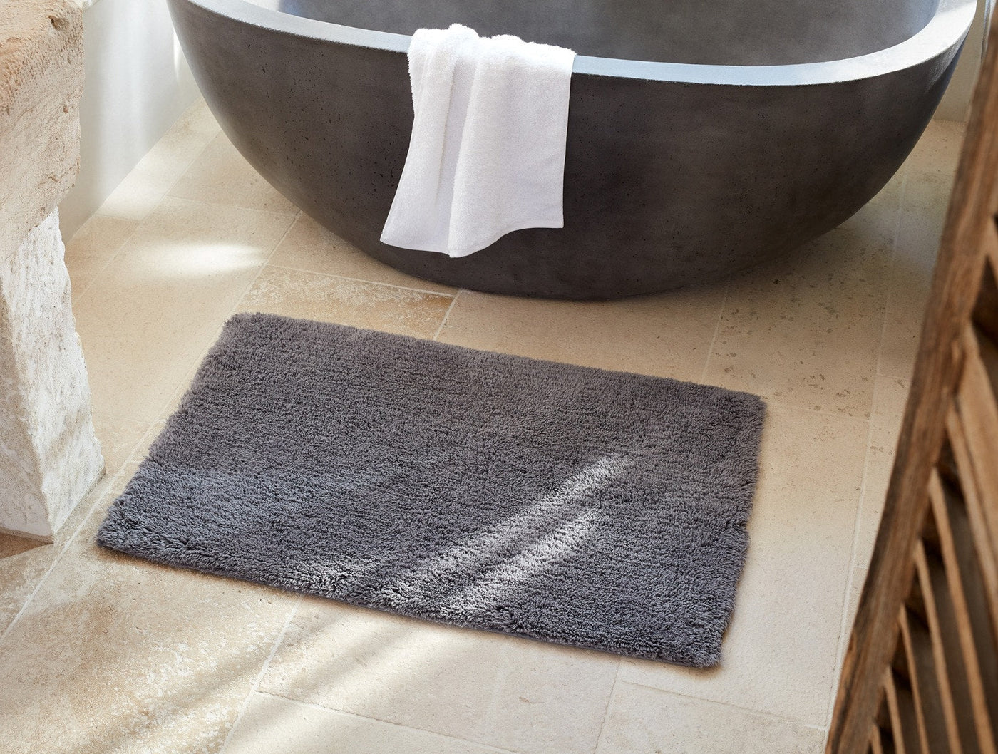 Coyuchi Shag bath rug in charcoal, styled on stone tile floor beside a freestanding tub.