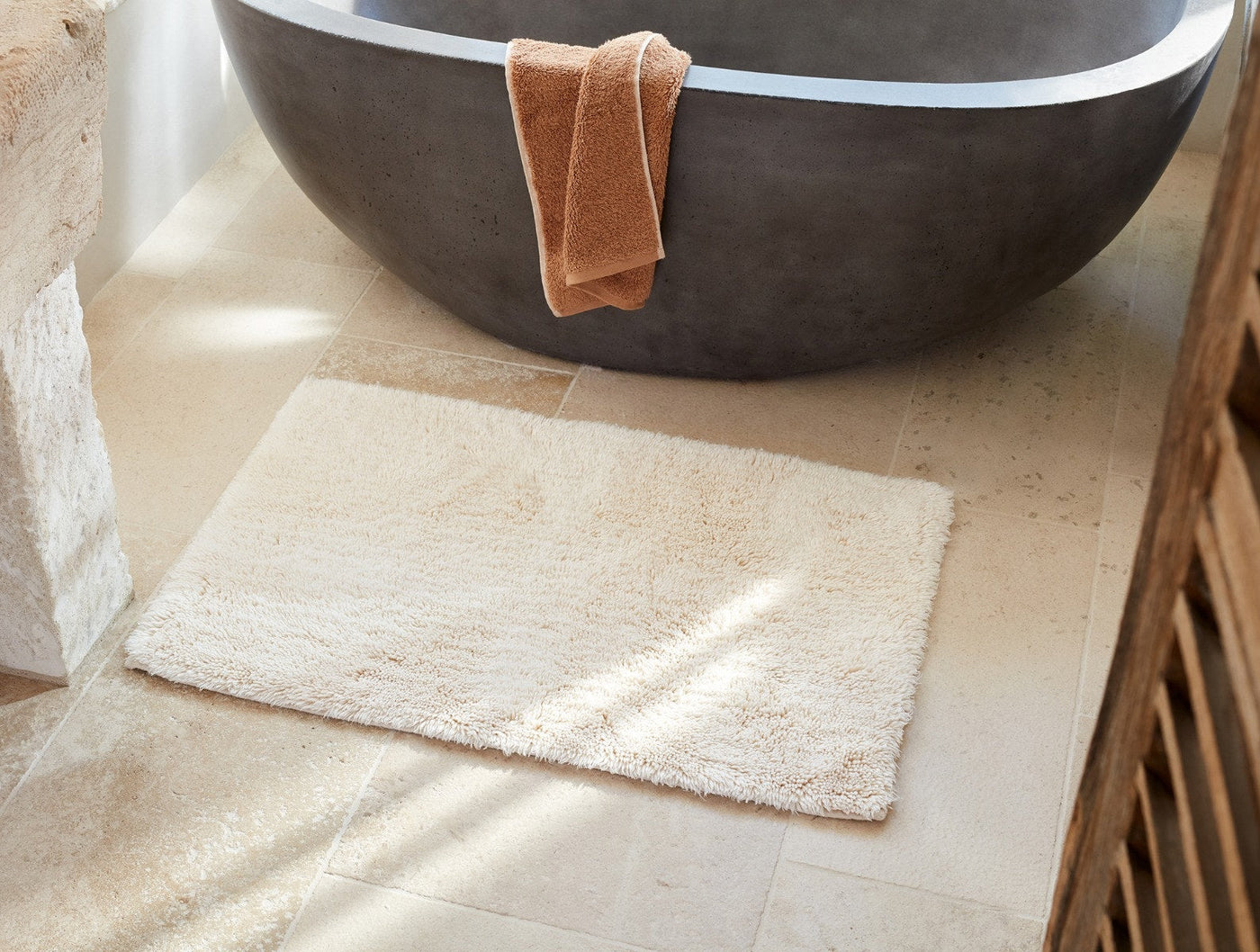 Coyuchi ivory shag bath rug on marble tile floor beside a dark stone freestanding tub.