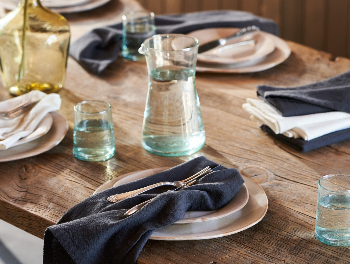 Navy linen napkins styled on a rustic wood table with glassware and place settings.