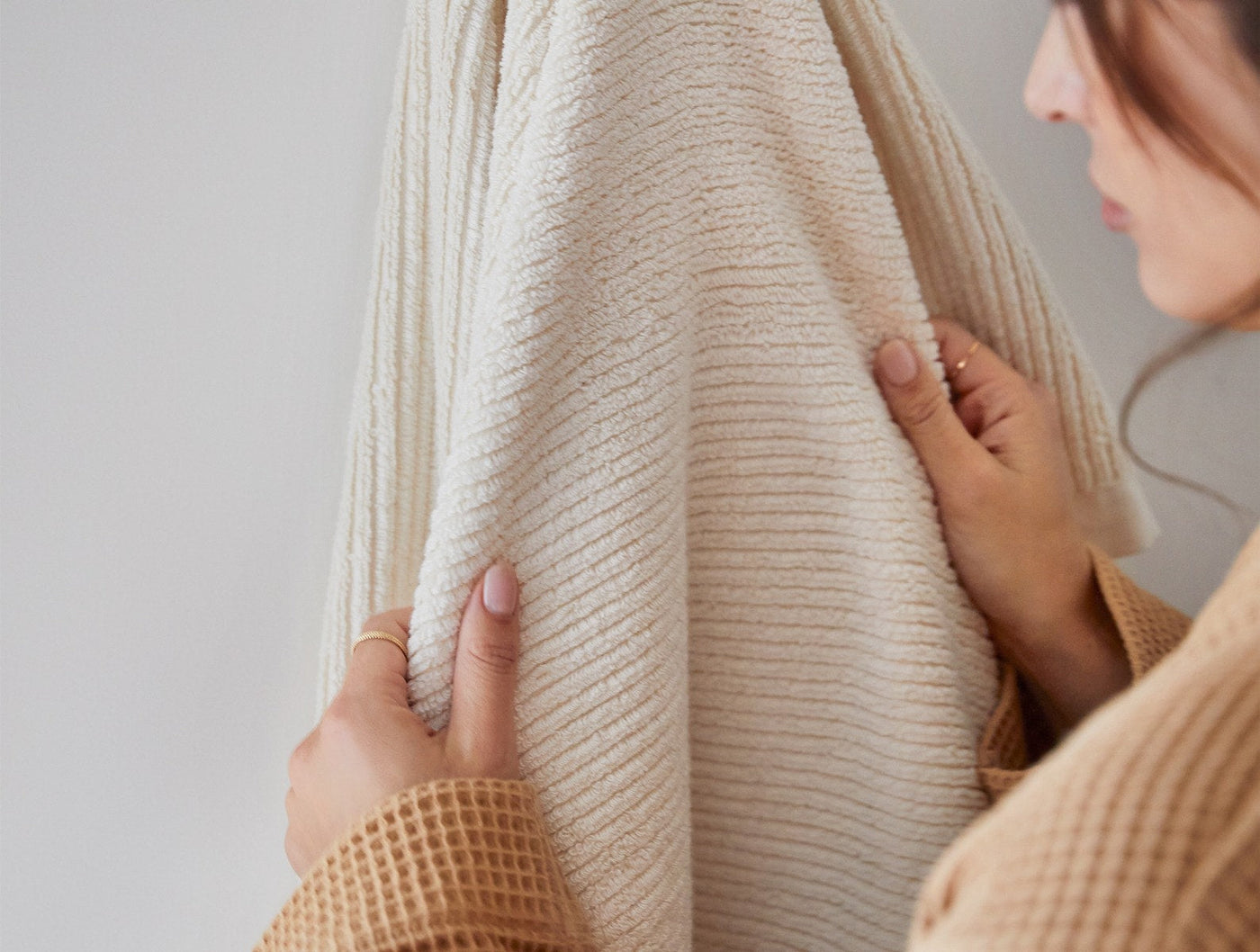 Close-up of hands holding a ribbed ivory Coyuchi Temescal towel, showing textured weave detail.
