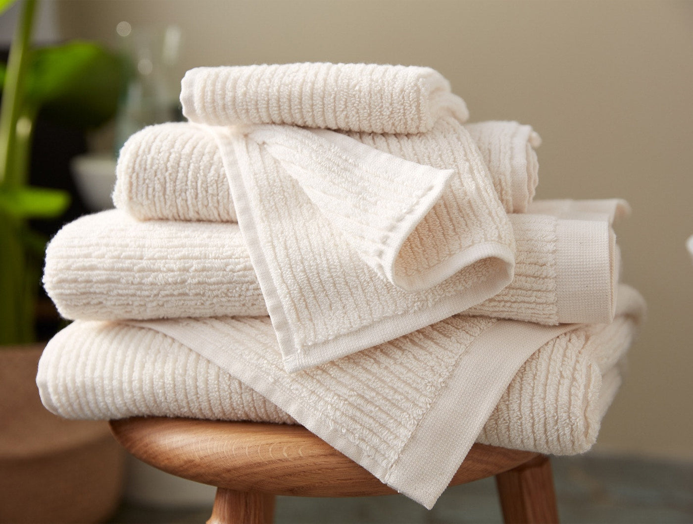 Close-up of stacked ivory ribbed Coyuchi Temescal towels in various sizes on a wooden stool.