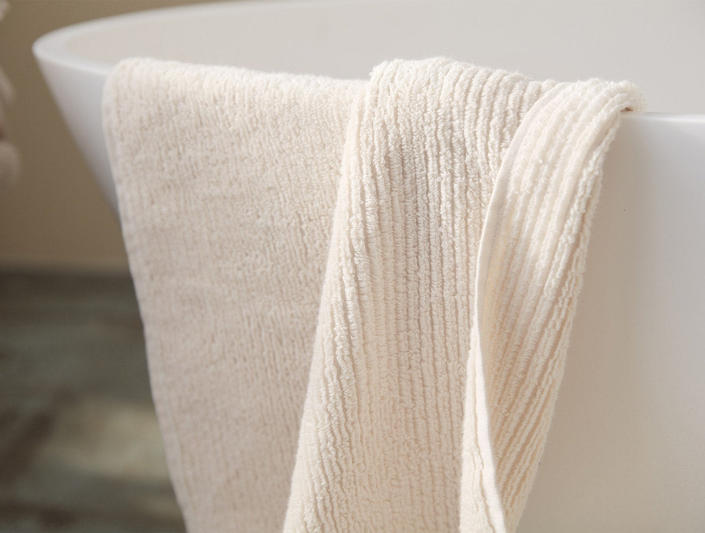 Ivory ribbed terry wash cloth draped over the edge of a freestanding bathtub.