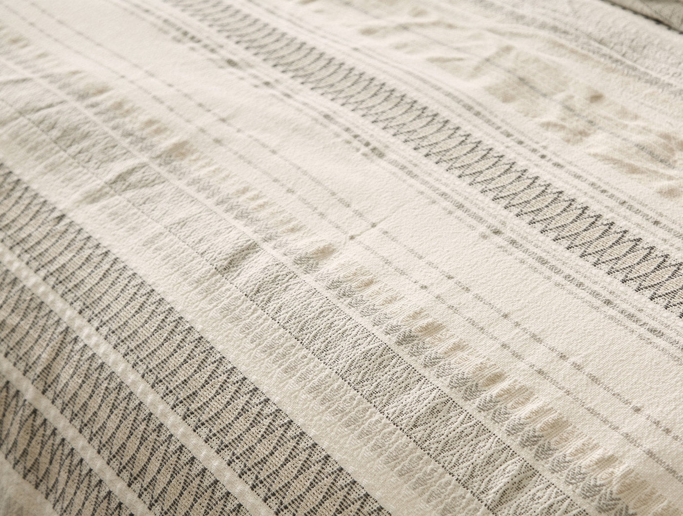 Close-up of Coyuchi Lost Coast duvet cover showing ivory woven stripes and textured stitch detail.