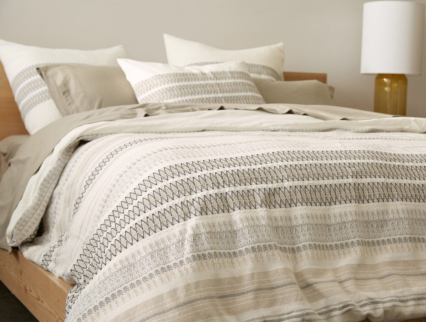 Coyuchi Lost Coast sham styled on bed, ivory with charcoal stripe embroidery detail.