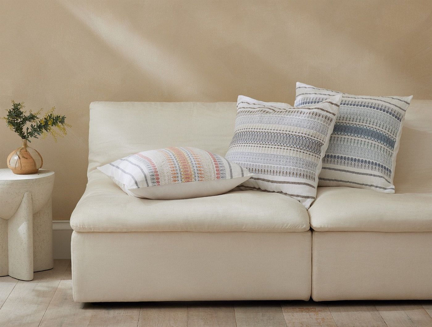 Coyuchi Lost Coast pillows styled on a cream sofa, showing small and large sizes with stripe pattern.