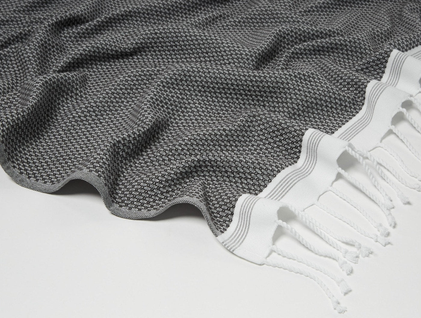 Close-up of Coyuchi Mediterranean guest towel in charcoal, showing woven texture and white fringe hem.