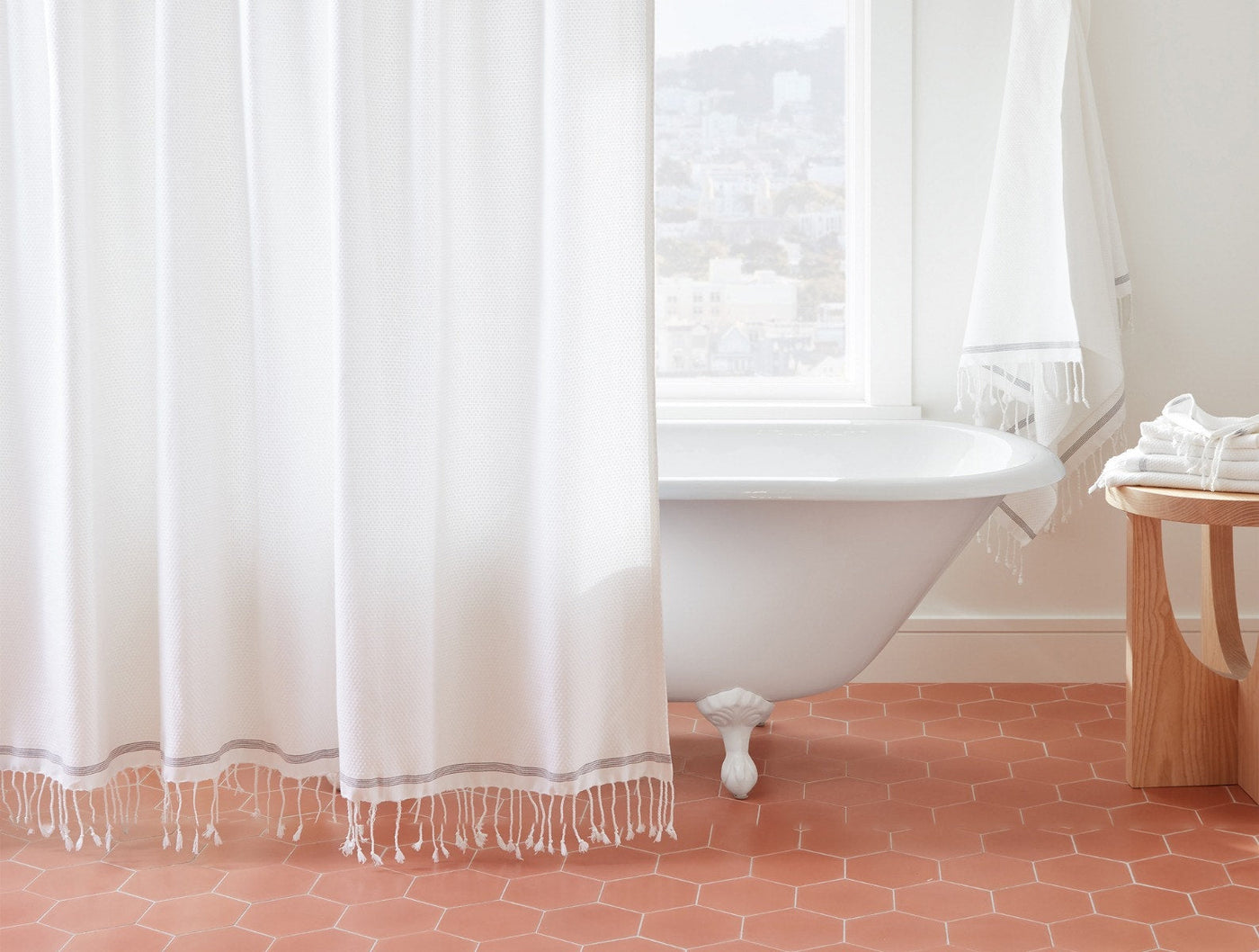 Coyuchi Mediterranean shower curtain in white with tassel hem, styled in a clawfoot tub bathroom.