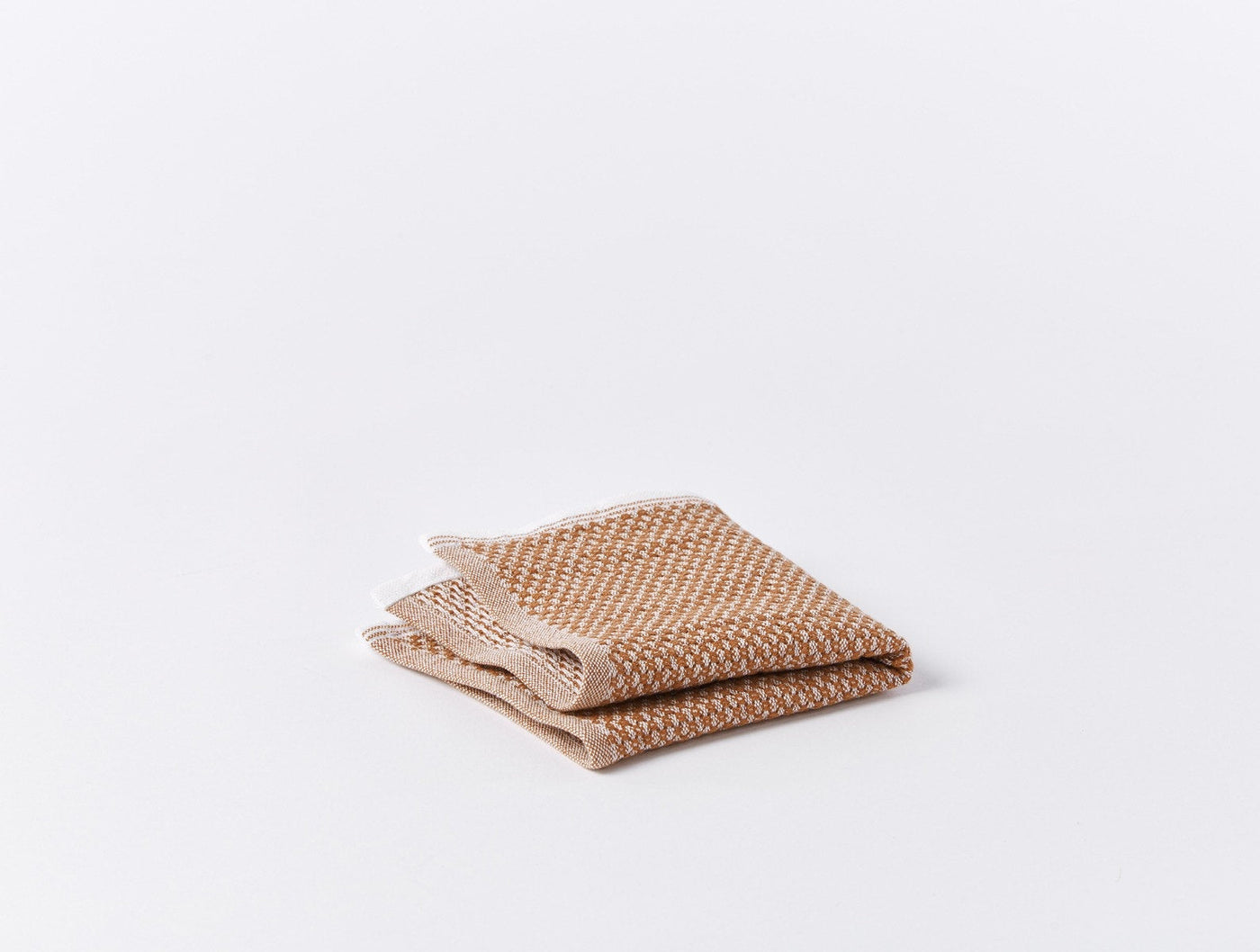 Two folded Coyuchi Mediterranean bath towels in terracotta and white woven texture, stacked on white surface.