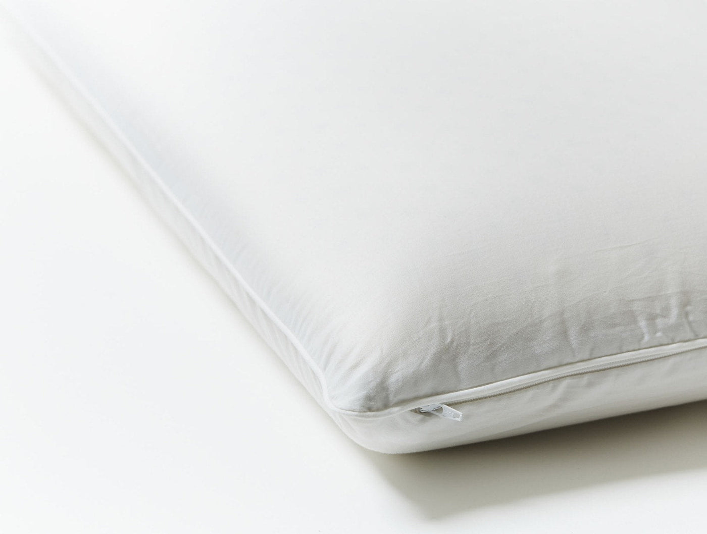 Corner detail of a white Coyuchi Latex pillow showing zipper closure and firm edge profile.