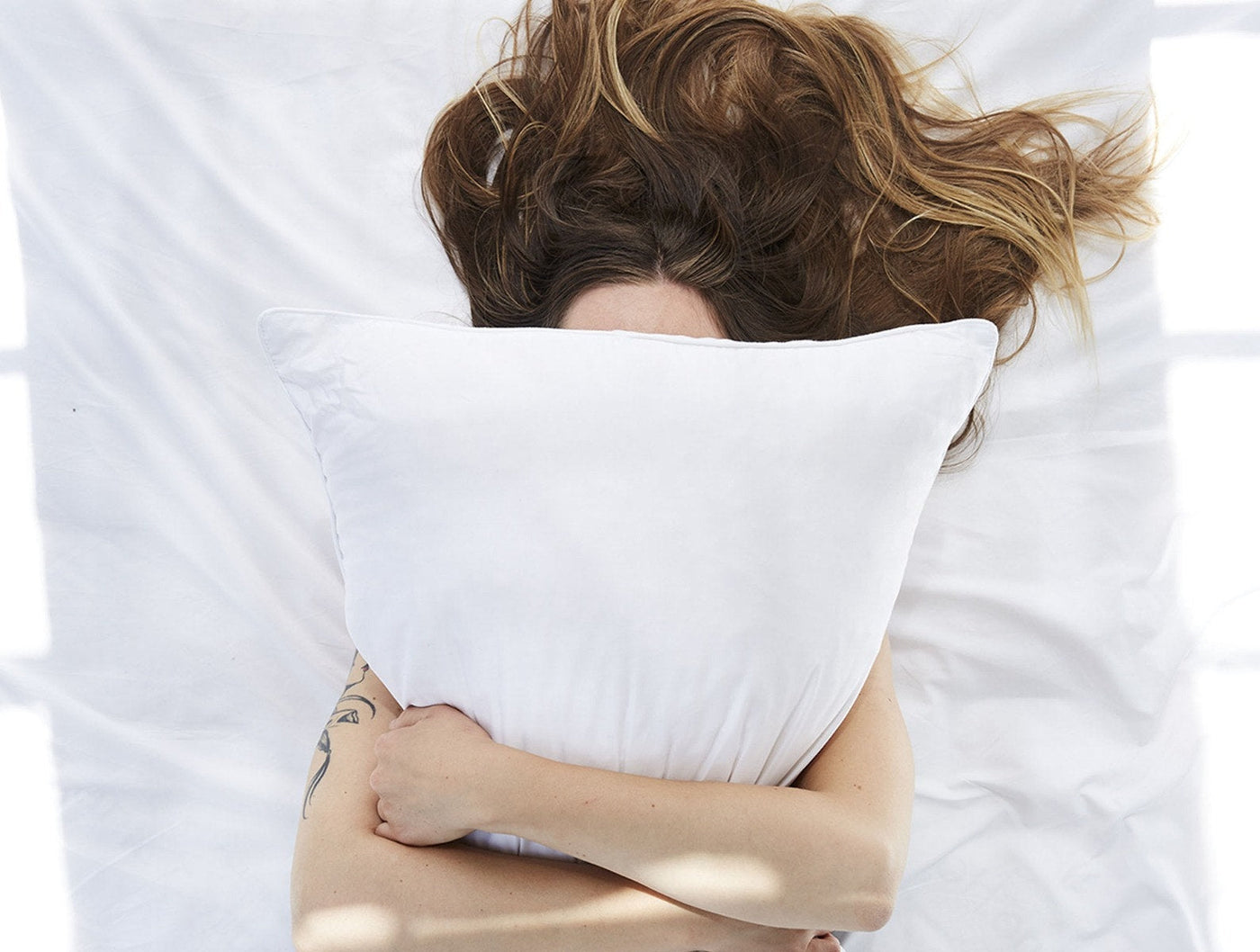 Woman lying on white bedding hugging a white Coyuchi Latex pillow to her face.