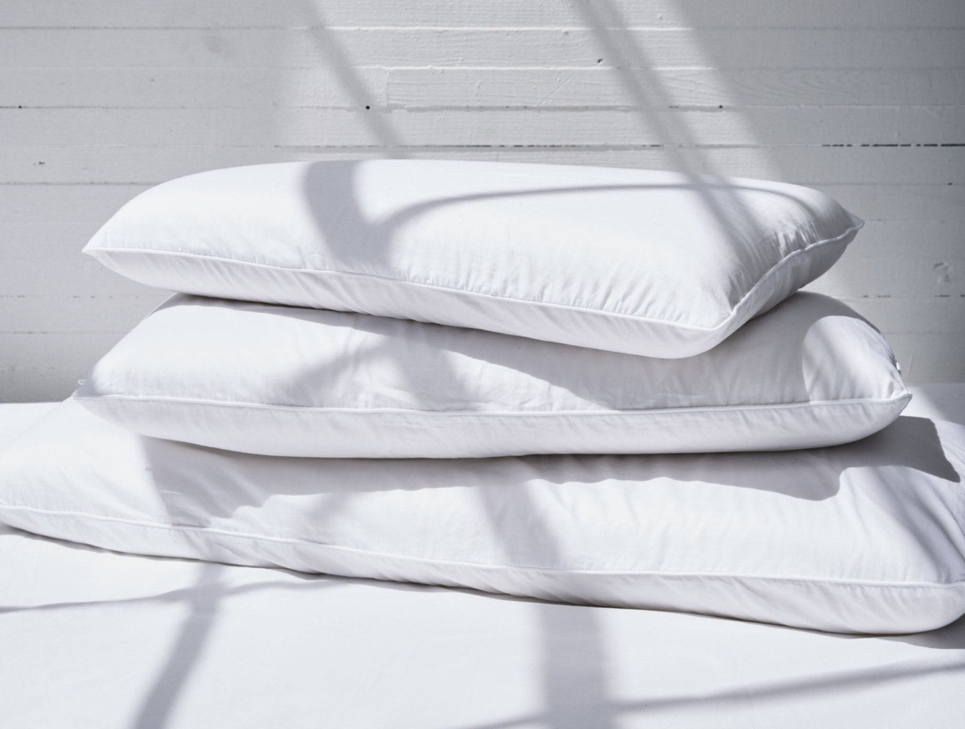 Three white Coyuchi latex pillows stacked in sunlight, showing size variation.