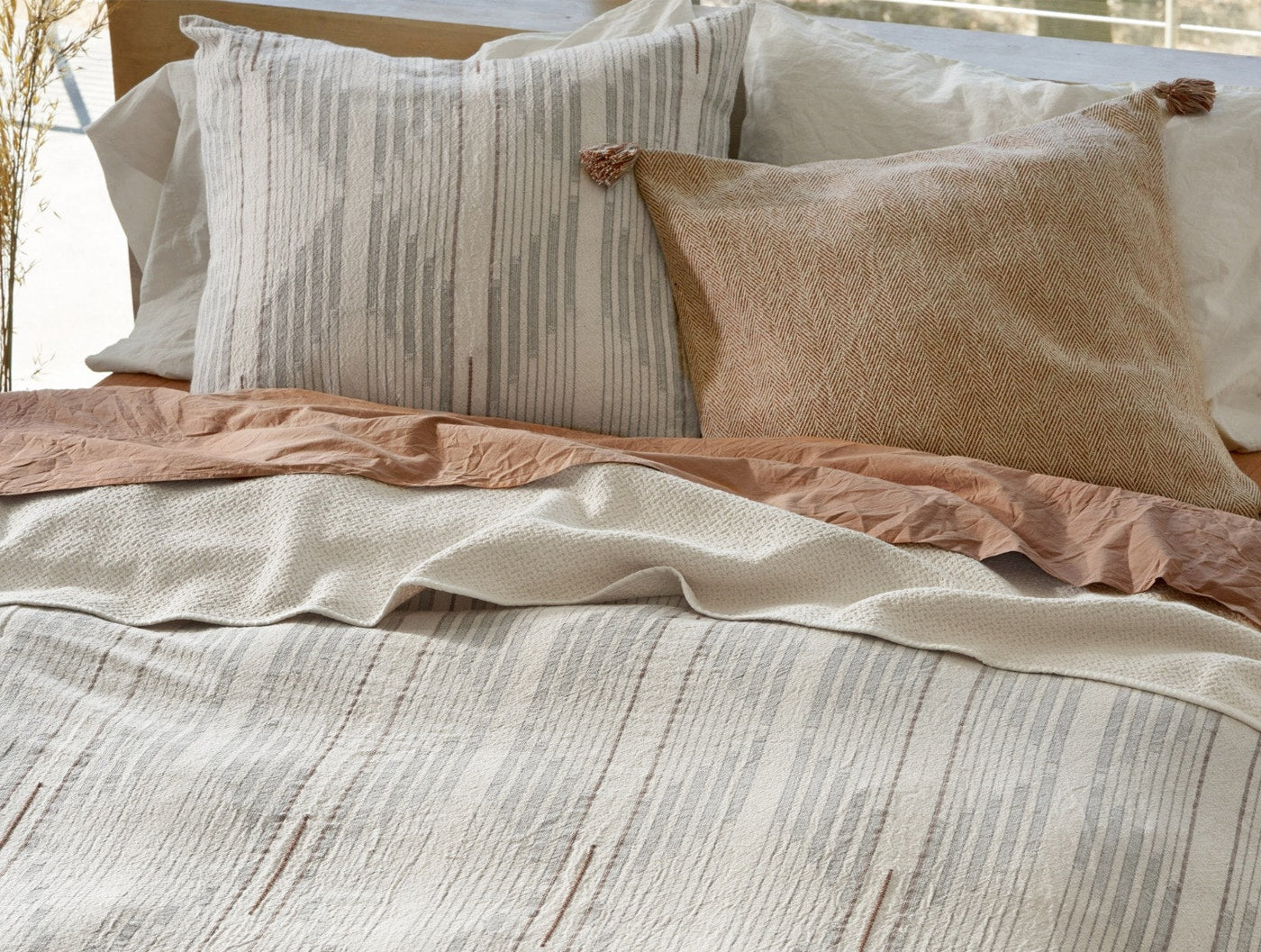 Close-up of Coyuchi Morelia sham in ivory with subtle gray stripe texture on styled bed.
