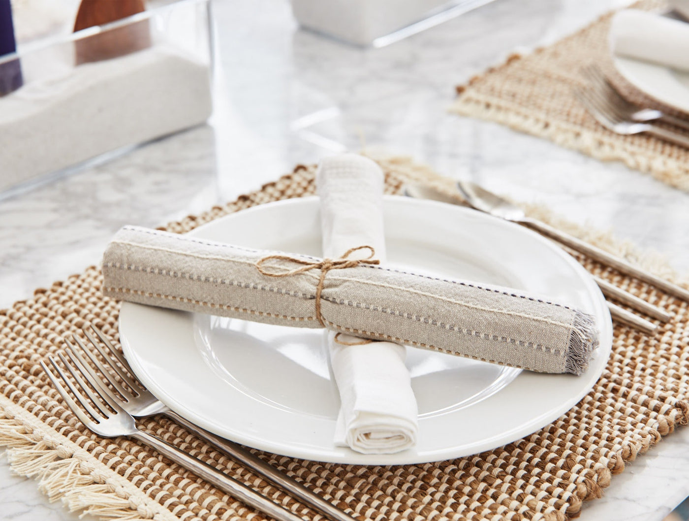 Coyuchi Fringe Stripe napkins rolled and tied with twine on white plate, woven placemat setting.