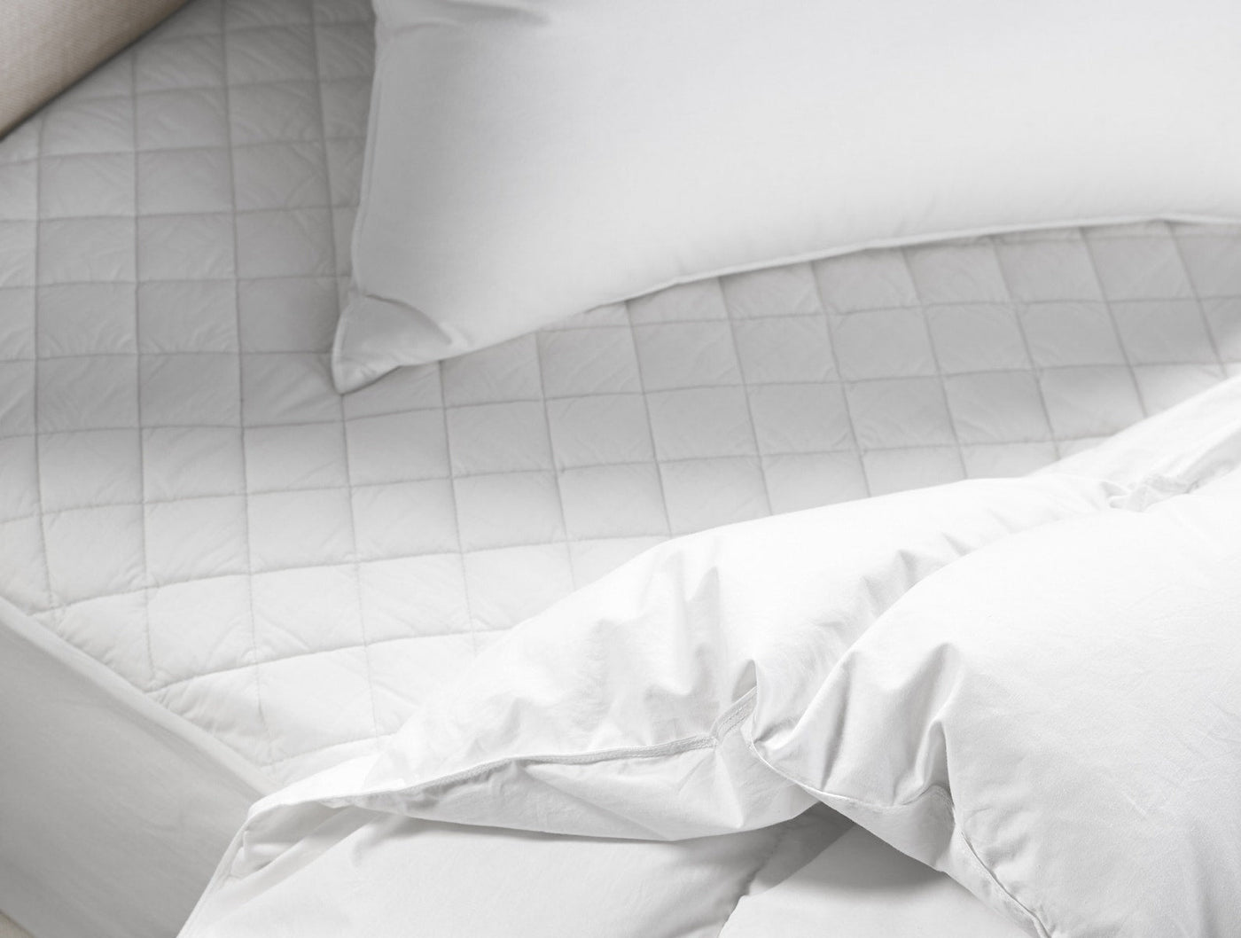 Close-up of white quilted Coyuchi mattress pad on bed with white pillow and duvet.