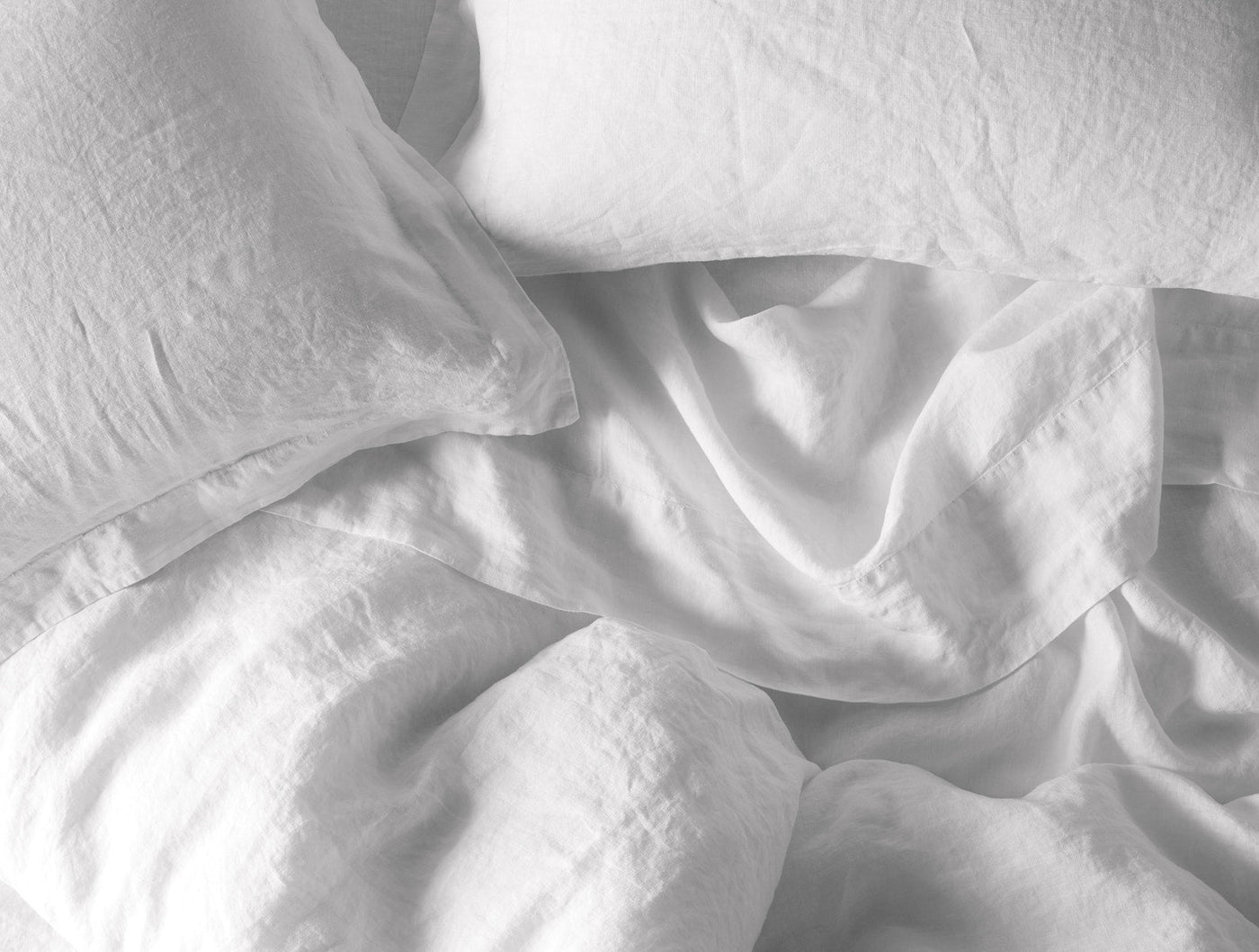 Overhead view of rumpled white Coyuchi linen sheets and pillowcase on a bed.