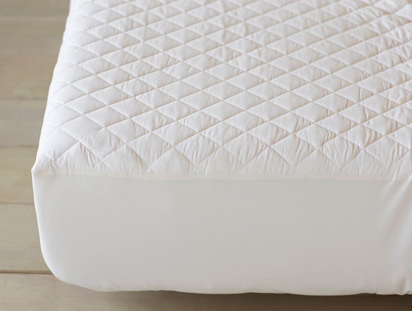Close-up of Coyuchi ivory quilted cotton mattress pad fitted on a mattress corner.