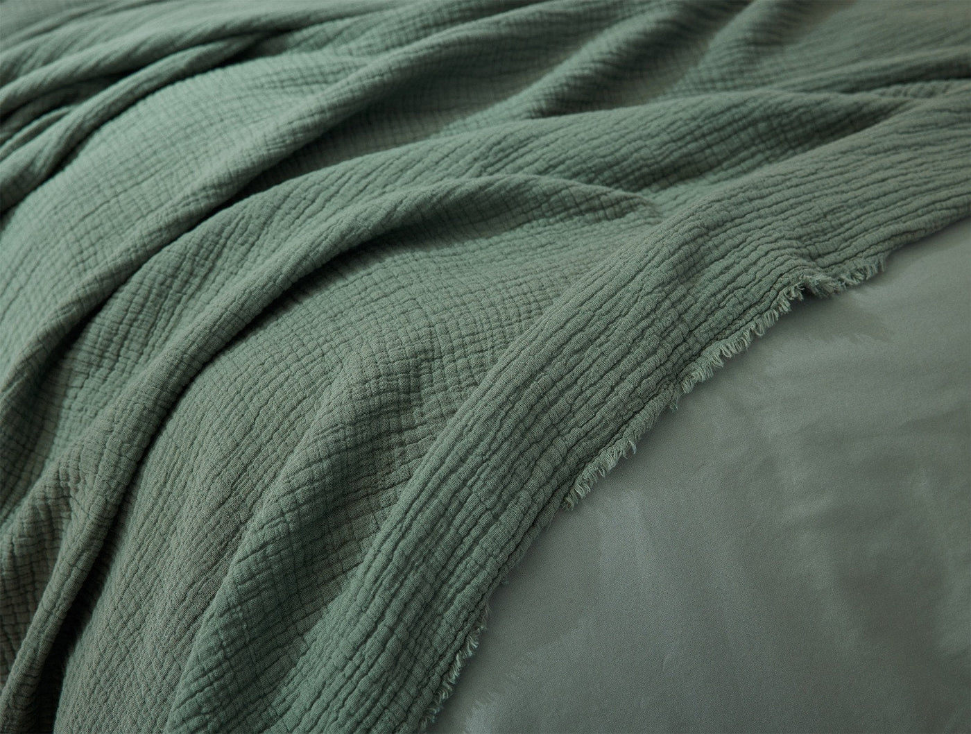 Close-up of sage green matelasse blanket with frayed hem draped over bedding.