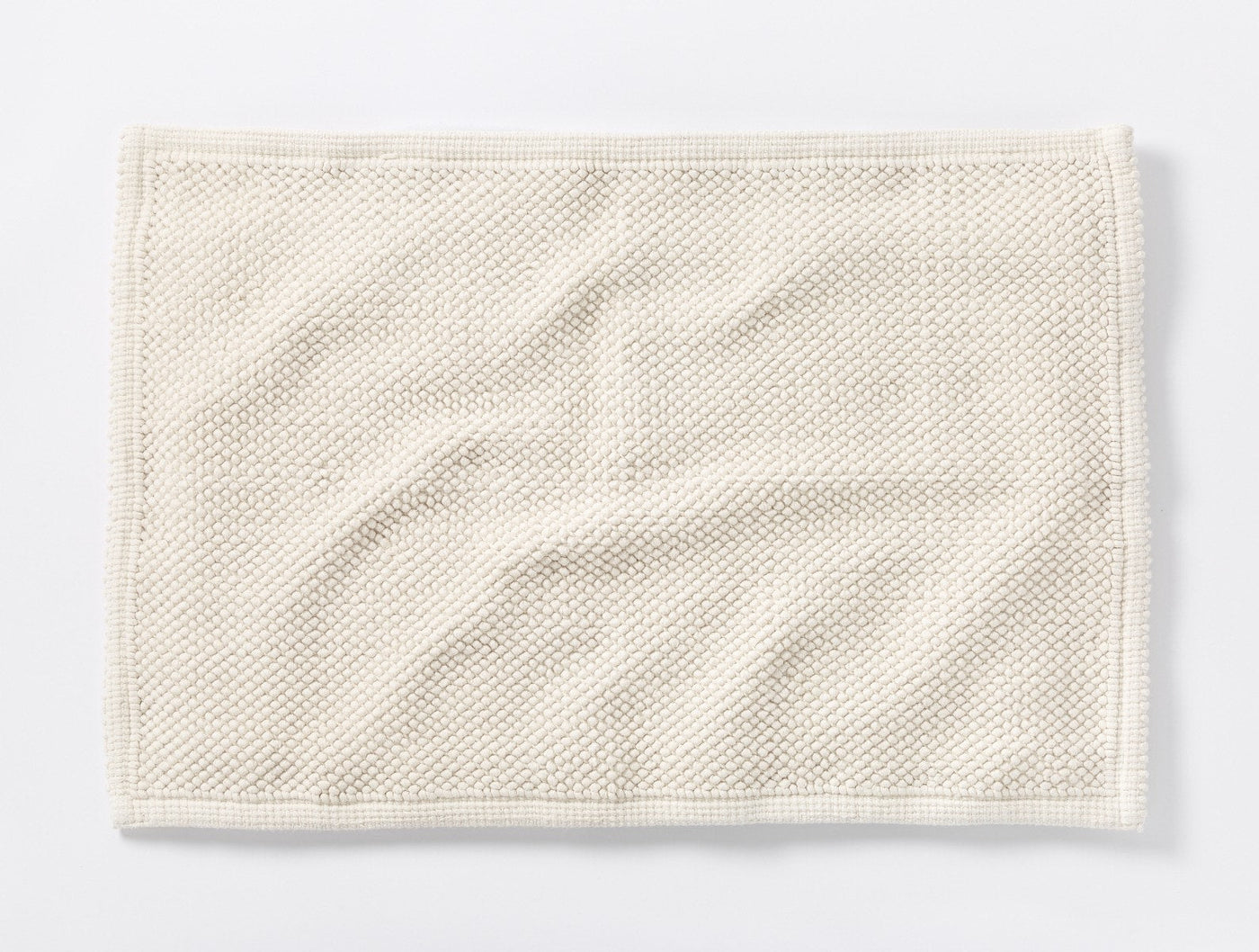 Overhead view of ivory Coyuchi Pebbled bath rug showing textured weave and natural drape.