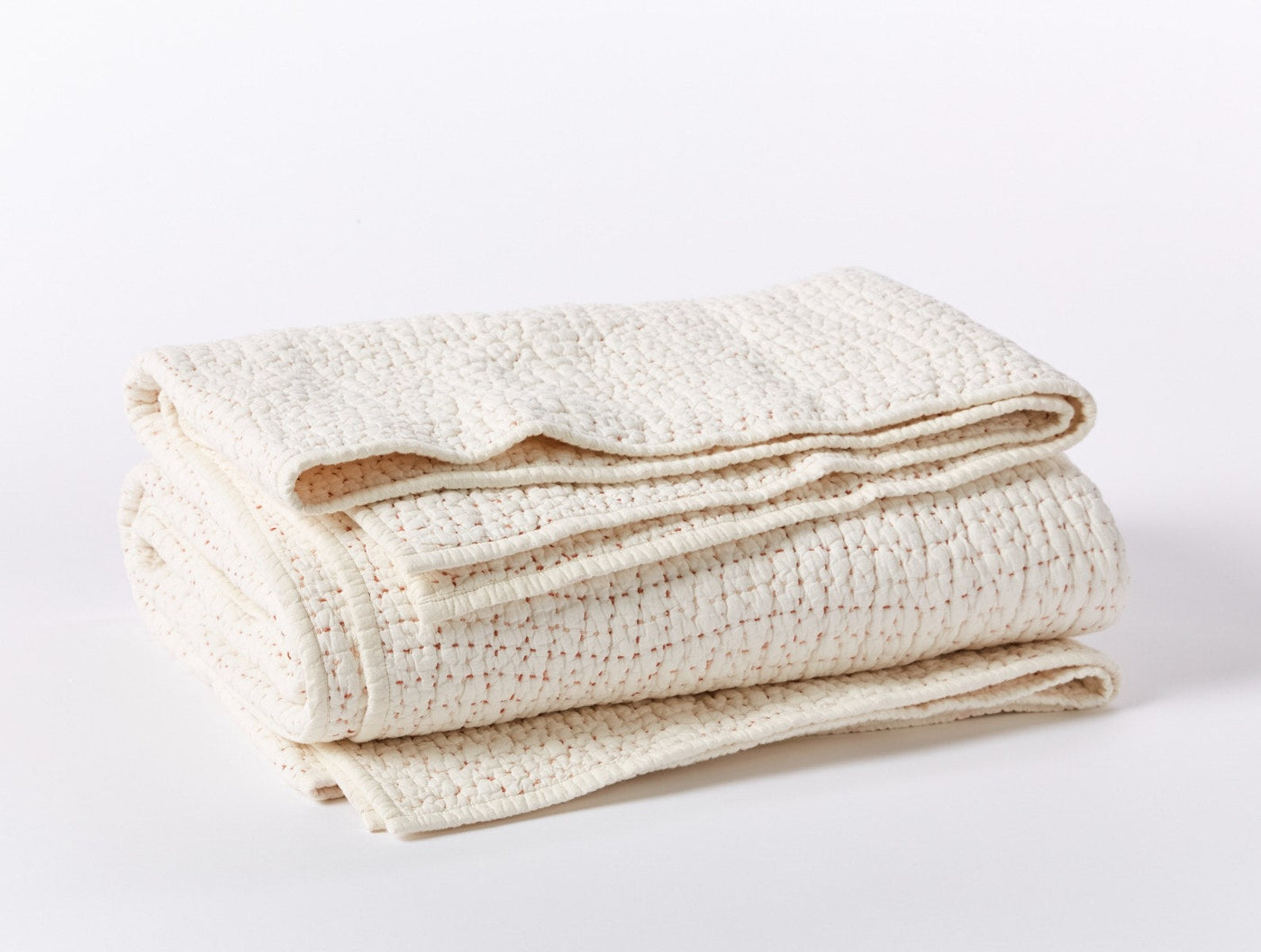 Coyuchi Pebbled Handstitched quilt folded, showing ivory textured weave and stitched hem detail.