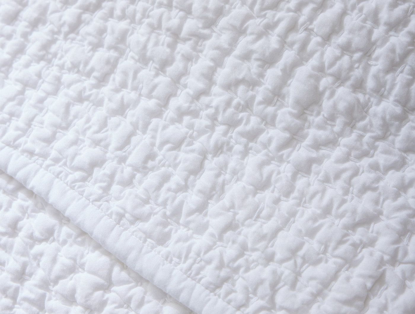 Close-up of Coyuchi Pebbled Handstitched quilt showing white textured stitching detail.