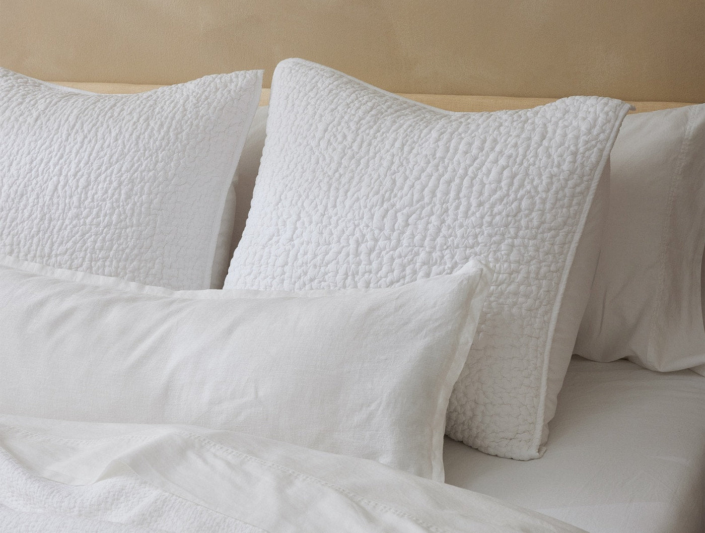 White quilted decorative pillows layered with relaxed linen shams on a styled bed.