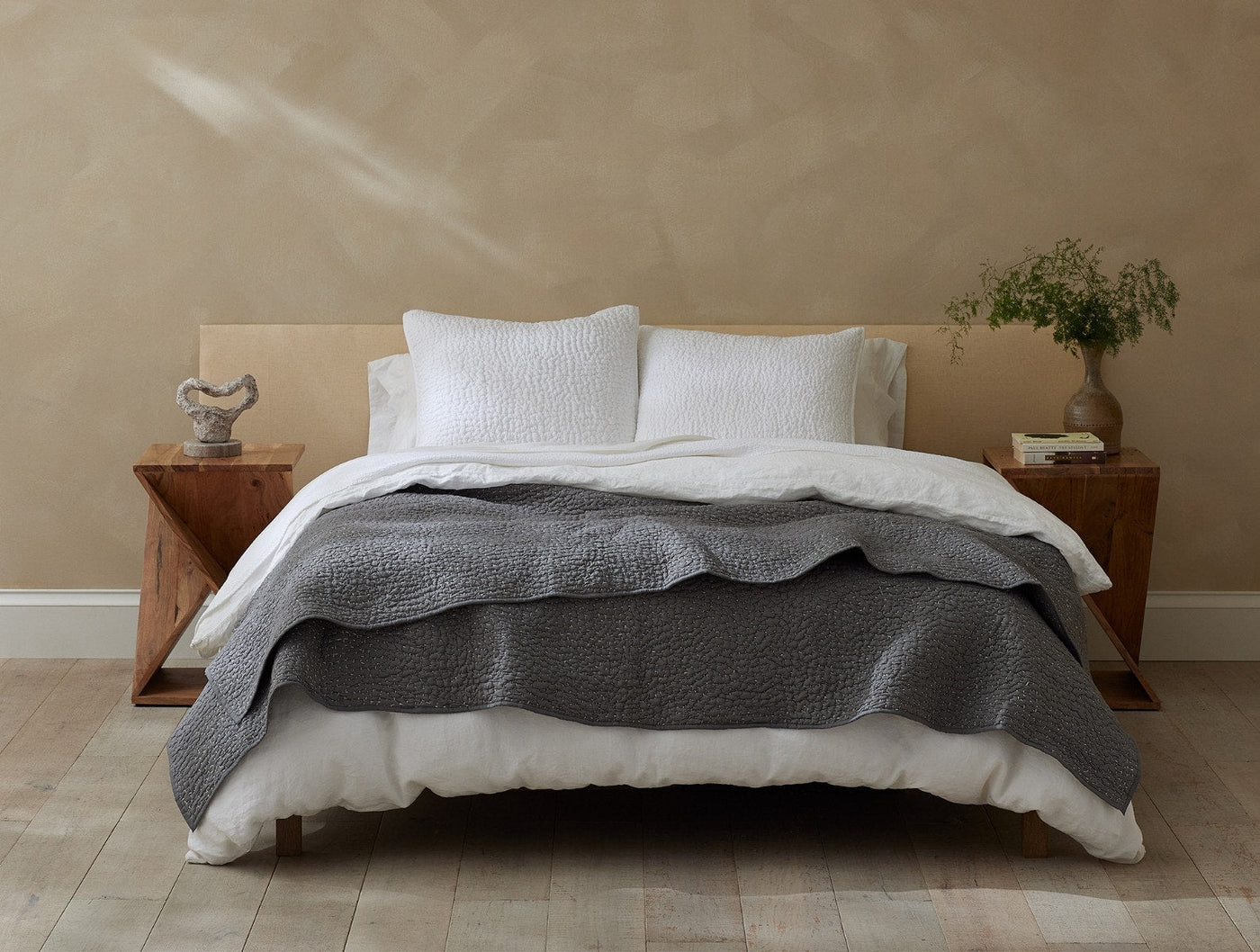 Charcoal Coyuchi quilt draped across foot of bed styled with white bedding and pillows.
