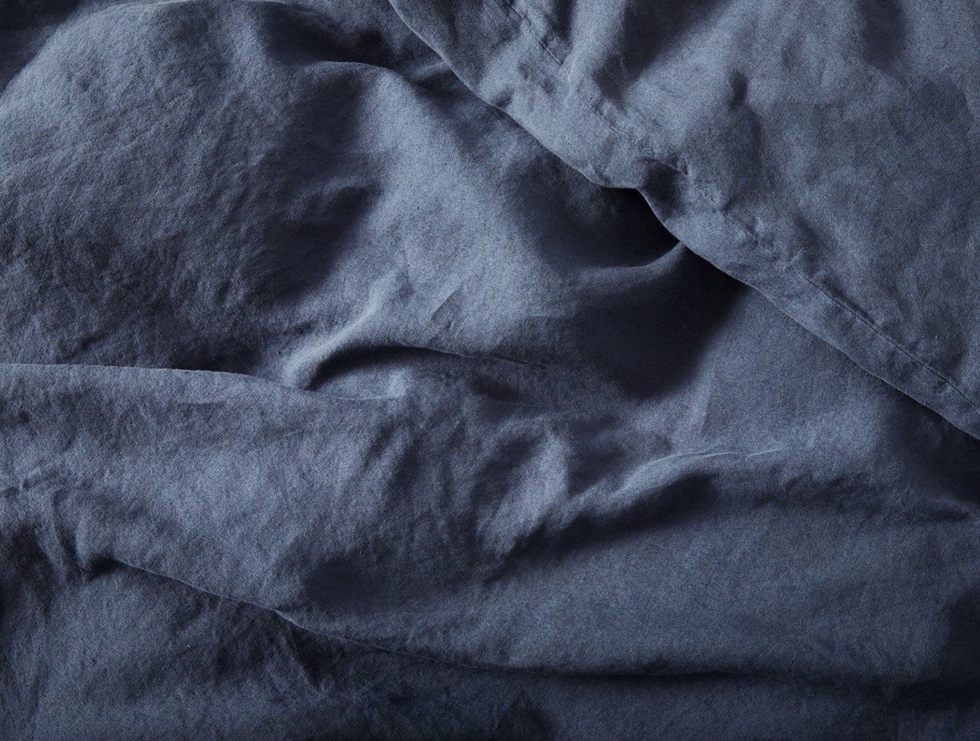 Close-up of rumpled slate blue linen fabric showing natural texture and drape.