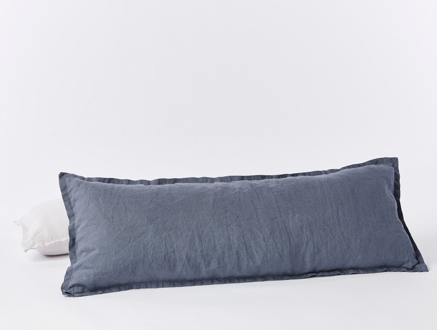 Slate blue Coyuchi long lumbar linen pillowcase with relaxed texture, white pillow peeking behind.