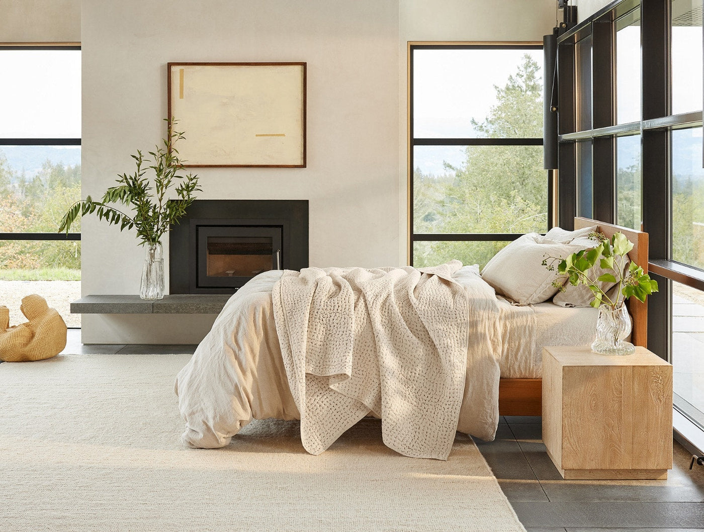 Coyuchi ivory pebbled quilt draped across bed in bright modern room with fireplace.