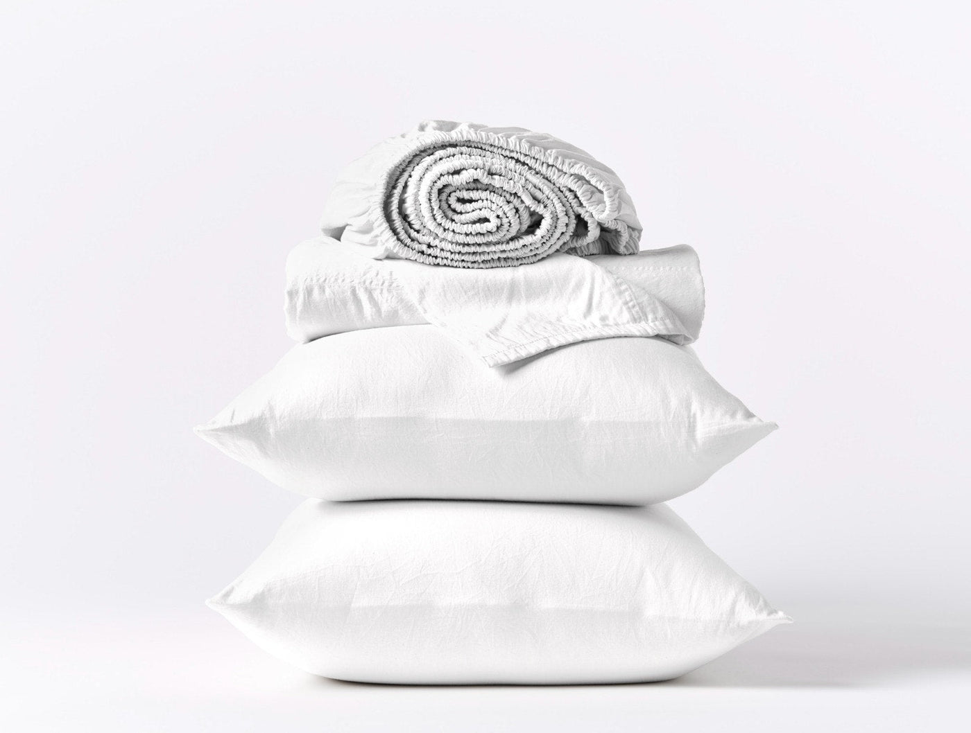 Coyuchi Cloud Soft Sateen sheet set in white, stacked pillows with rolled sheets.