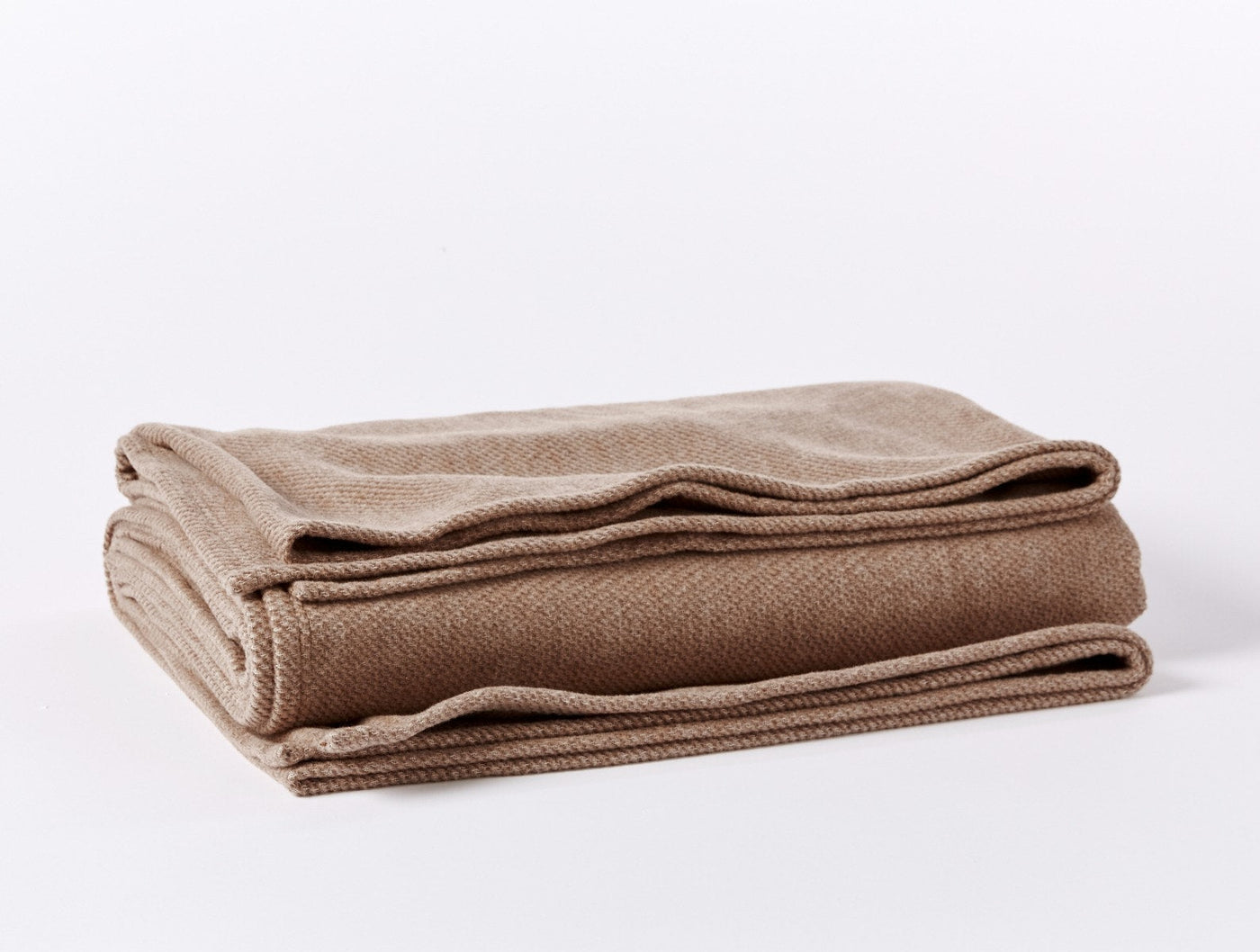 Camel herringbone-weave blanket folded and stacked, showing textured edge detail.