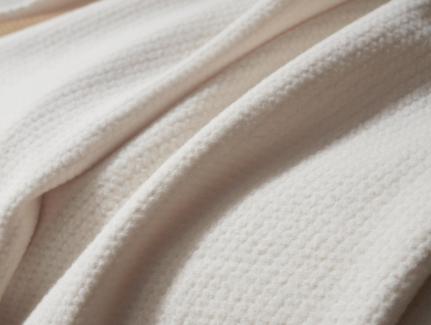 Close-up of ivory Coyuchi Sequoia blanket showing soft waffle-knit texture and draped folds.