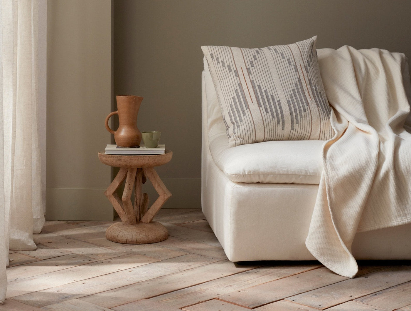 Ivory Coyuchi Sequoia blanket draped over a cream chair beside a sculptural wood side table.