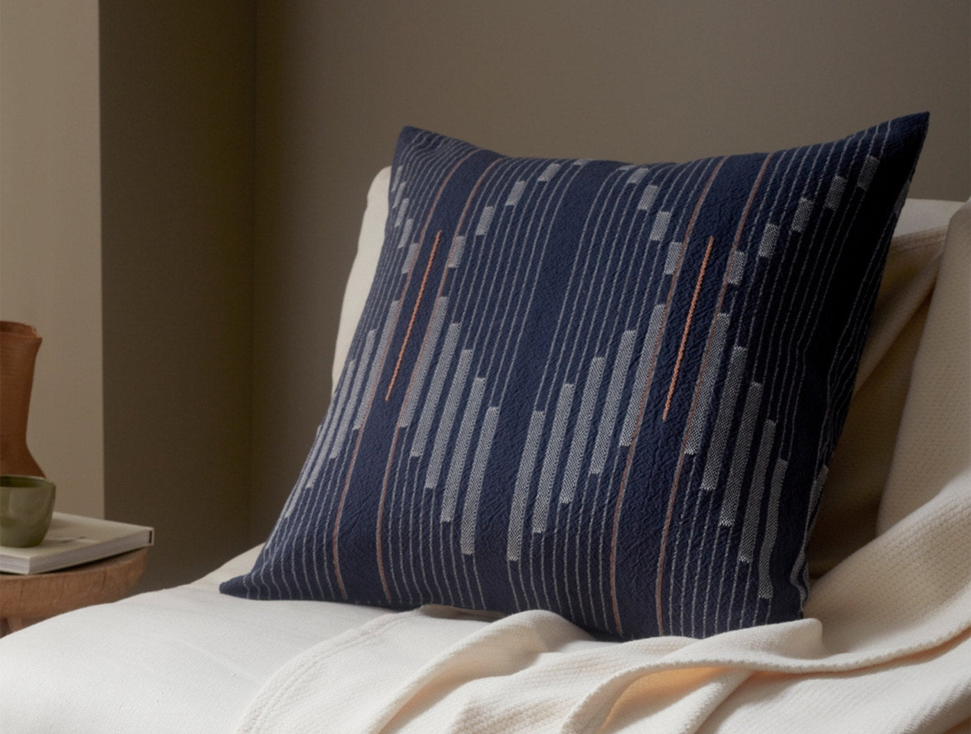 Coyuchi Morelia pillow in navy, styled on a bed with ivory throw, geometric stripe weave detail.