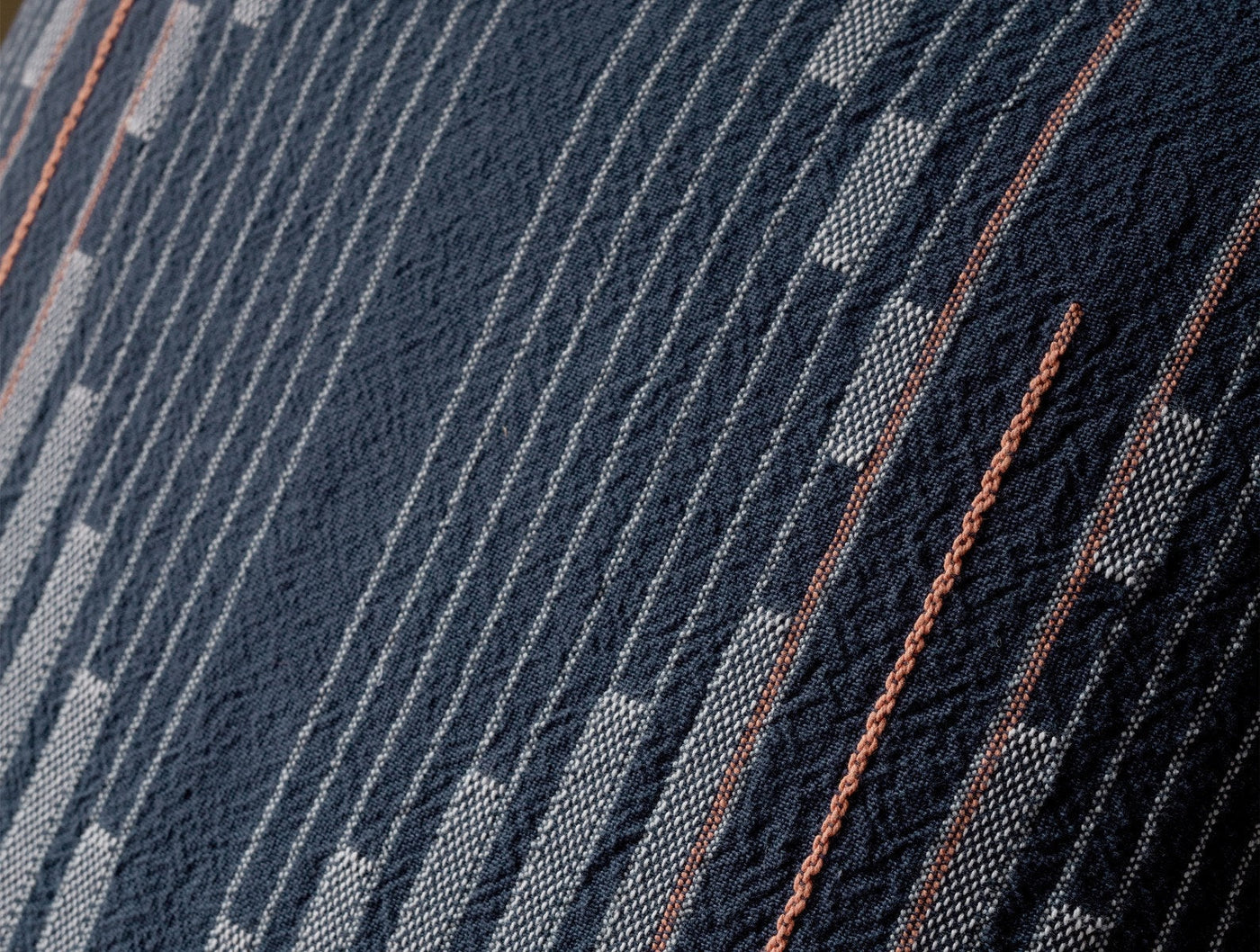 Close-up of Coyuchi Morelia pillow's navy woven textile with geometric patterns and rust stripe accents.