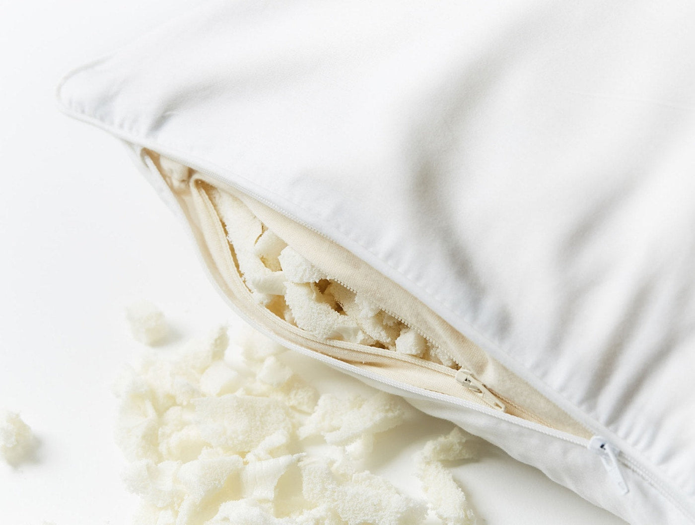 White Coyuchi latex pillow unzipped, revealing shredded latex fill spilling out.