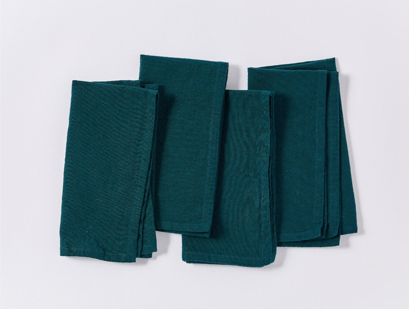 Four folded Coyuchi Sonoma teal linen napkins arranged flat, showing textured weave detail.