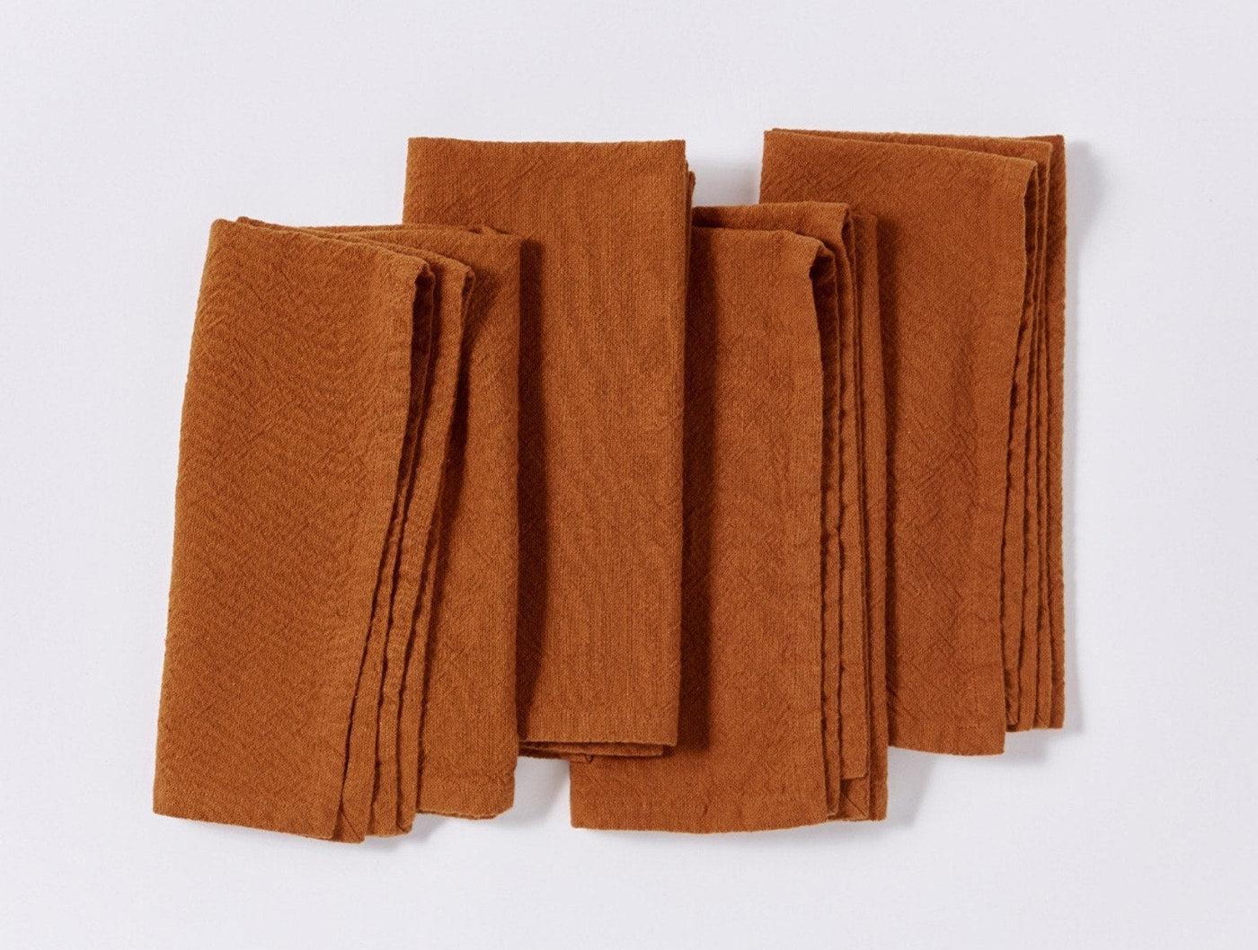 Close-up of four folded Coyuchi Sonoma Textured napkins in rust, showing woven texture detail.