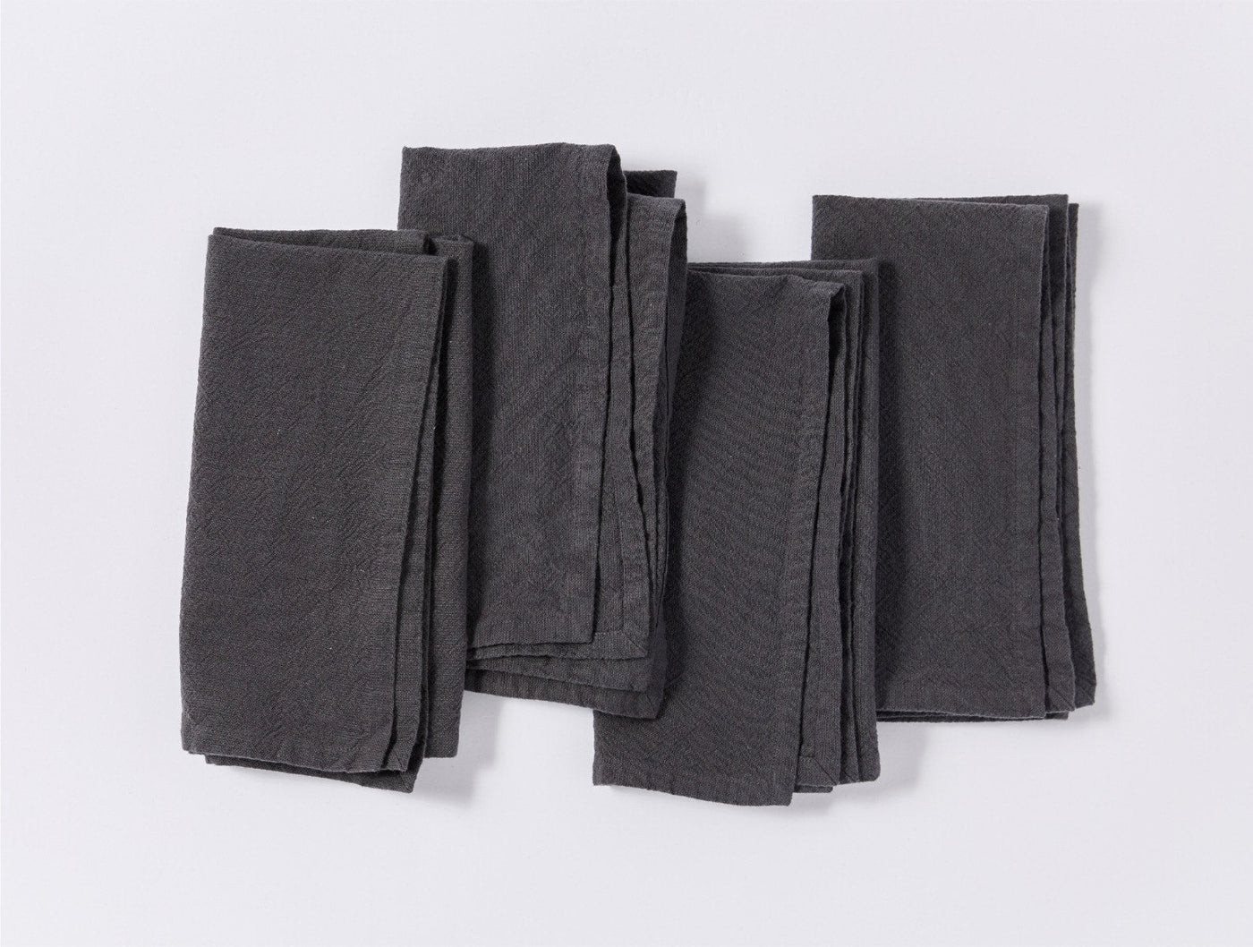 Four folded Coyuchi Sonoma Textured linen napkins in charcoal, fanned arrangement on white.