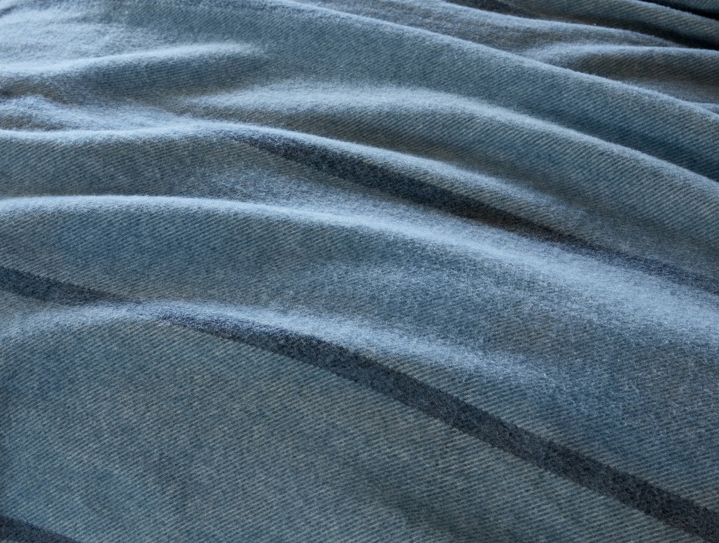 Close-up of draped slate blue Coyuchi Tahoe Wool throw, showing soft herringbone weave texture.