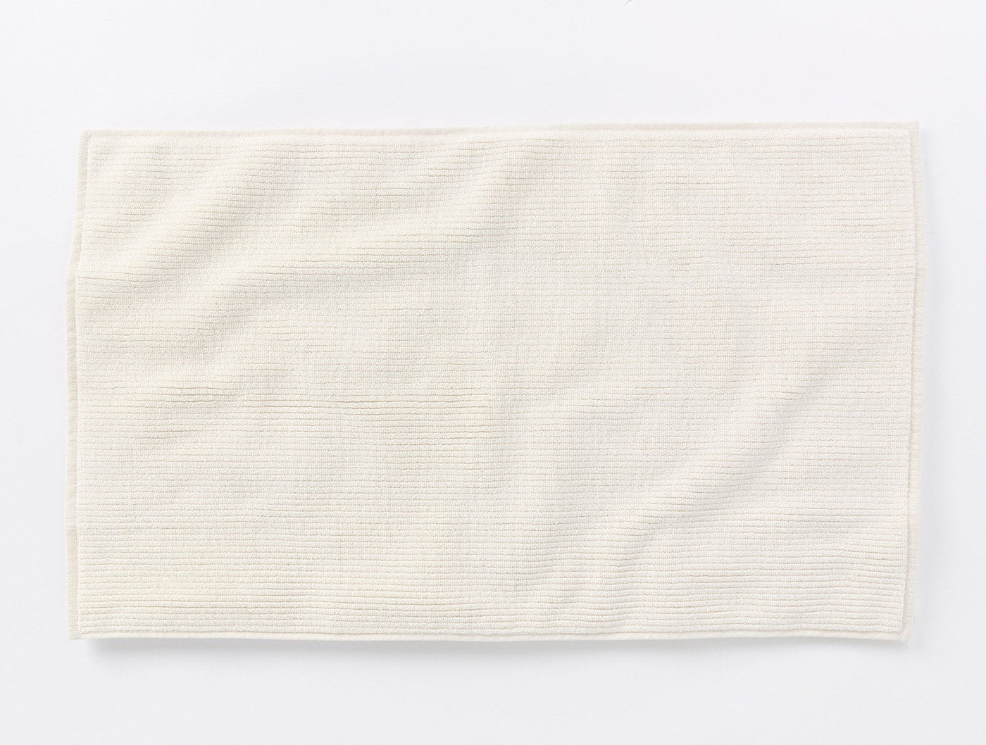 Coyuchi Temescal Ribbed bath rug in ivory, showing ribbed texture and draped flat lay.