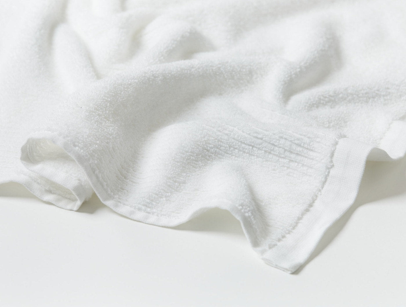 Close-up of white ribbed terry wash cloth with hemmed edge, draped on white surface.