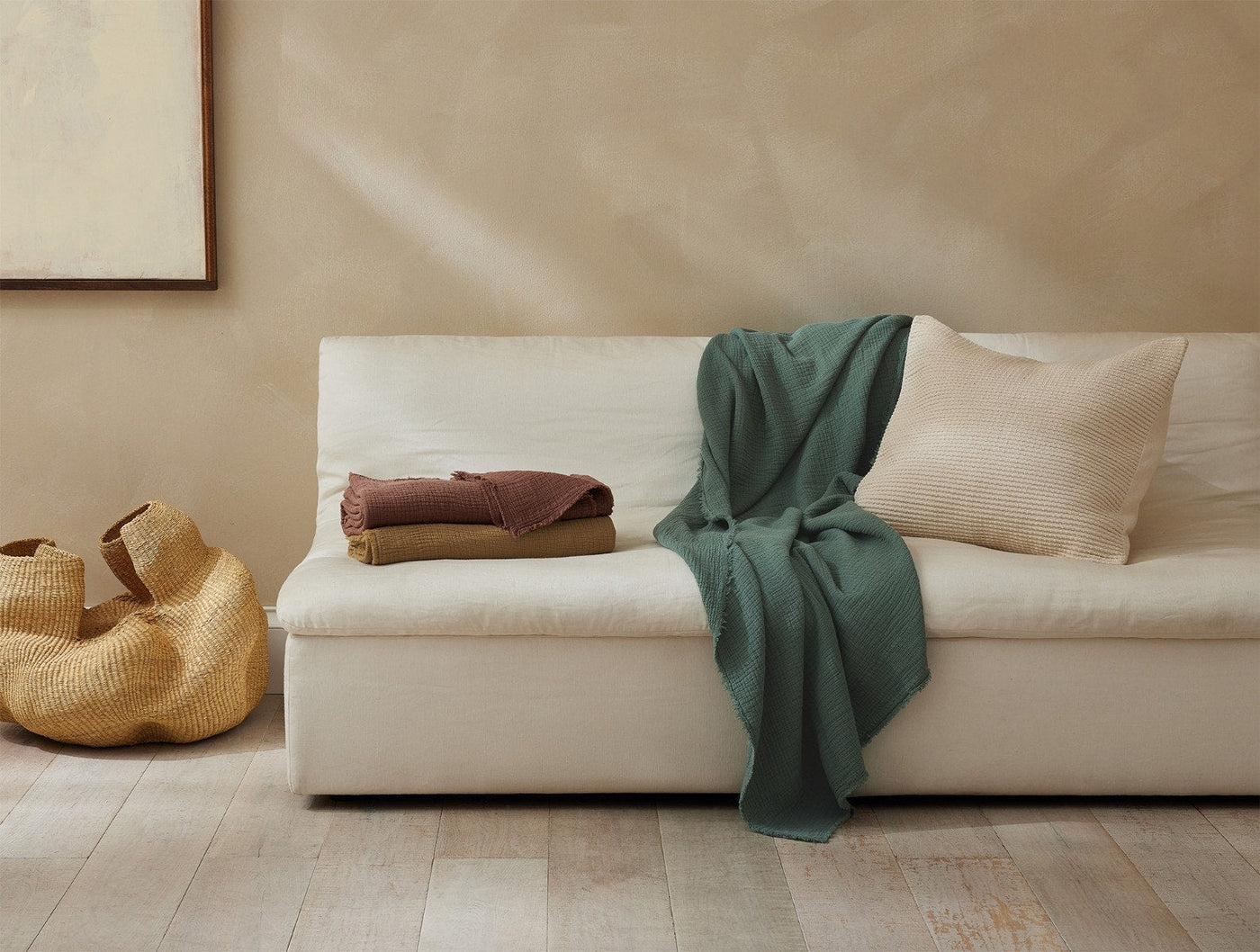 Green matelasse throw draped over cream sofa, with folded throws and woven basket nearby.